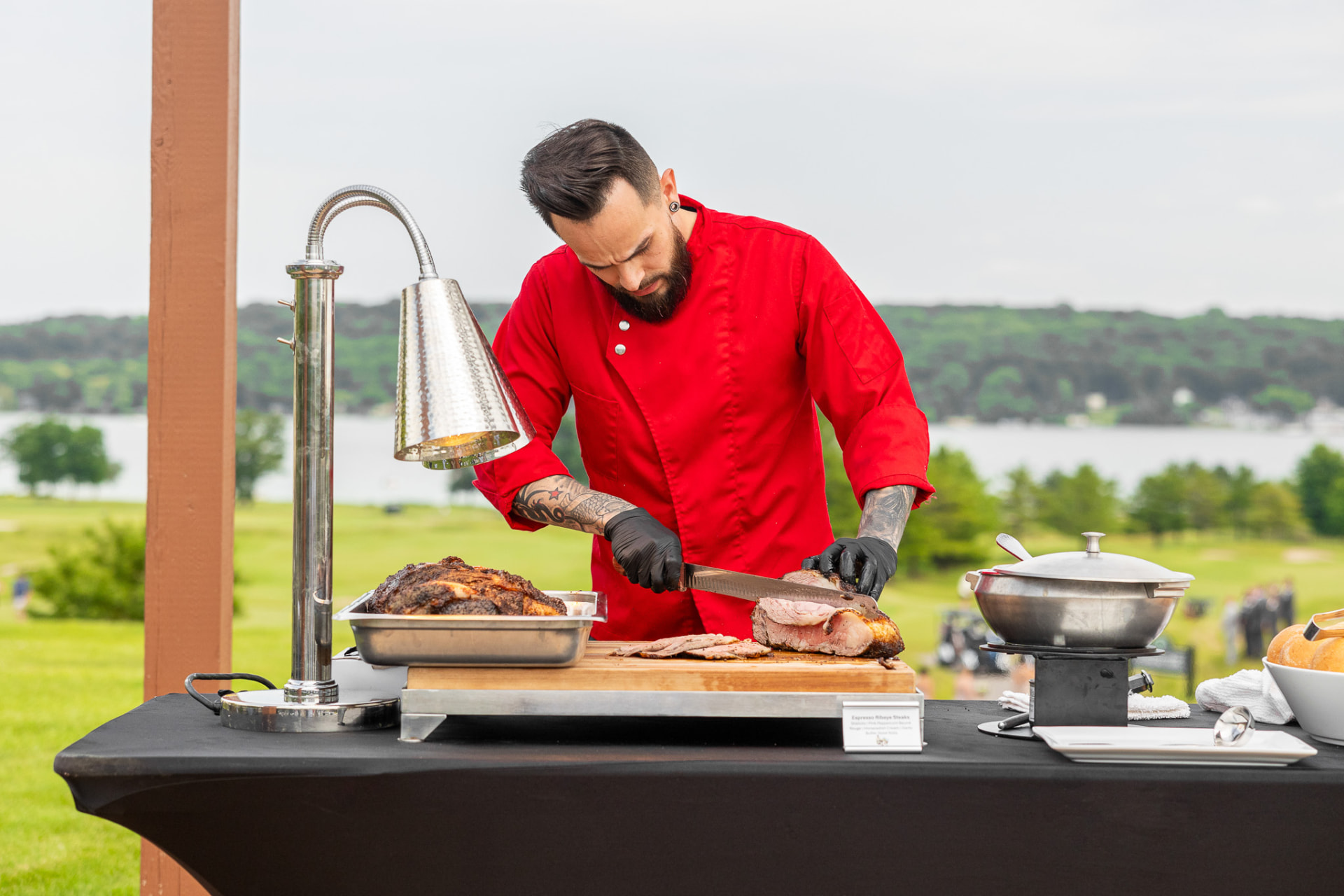 Fairchild chef carving espresso ribeye at an outdoor lakeside station